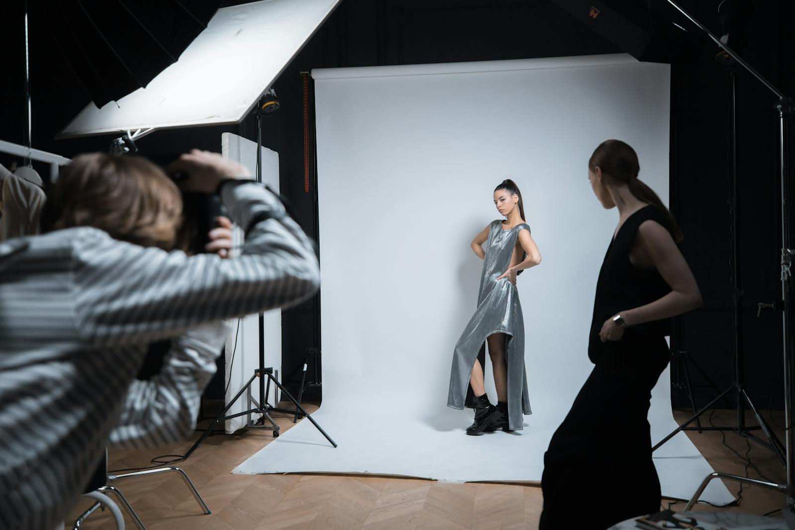 A working set in the JAMES VISUALS NIGERIA studio — two stylists pinning a garment on a model while a photographer reviews tethered captures on a calibrated monitor.